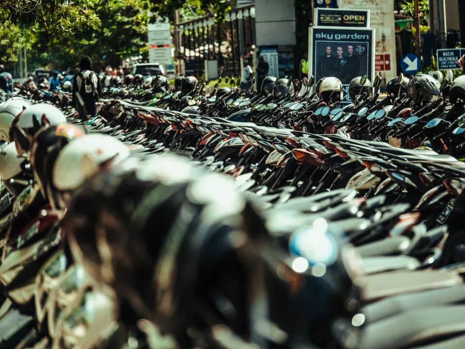 Fila de scooters estacionadas lado a lado com capacetes pendurados