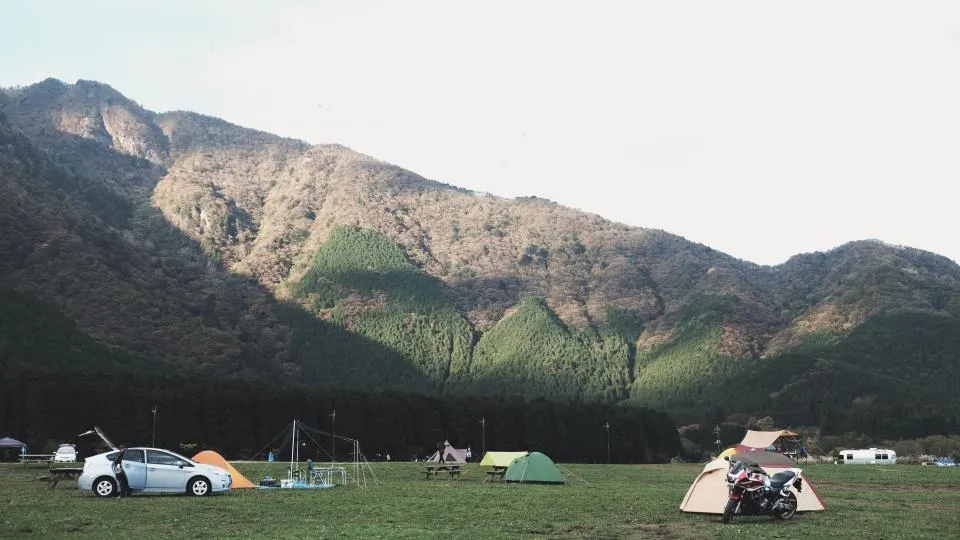 Mota estacionada junto a uma tenda de campismo ao pé de uma encosta florestal
