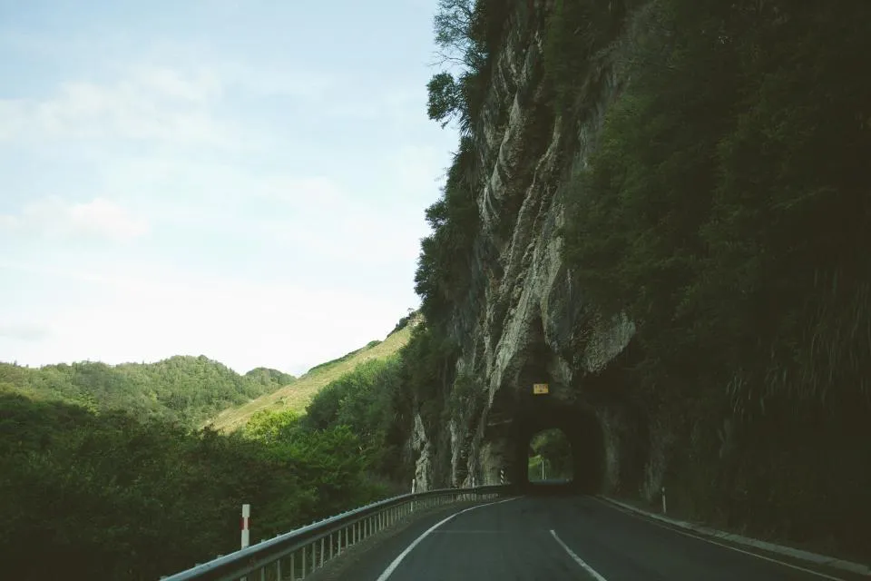 Estrada de montanha com túnel escavado na rocha e vegetação