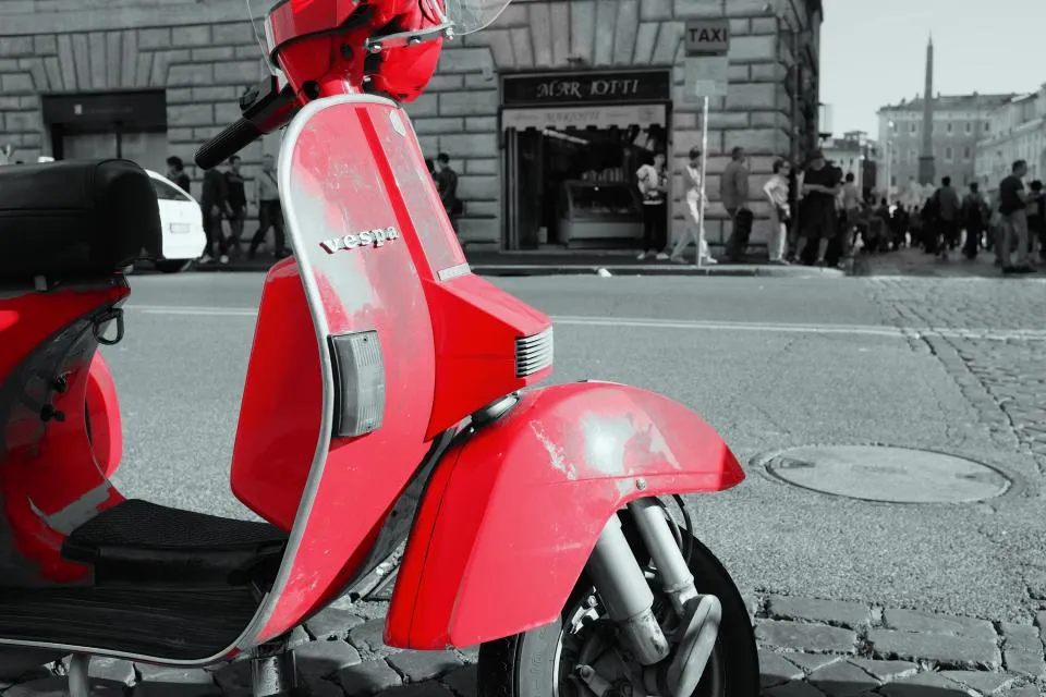 Scooter Vespa vermelha estacionada numa rua com calçada