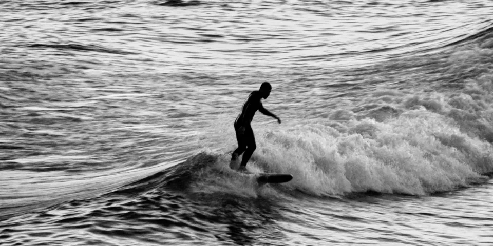Silhueta de um surfista numa onda em tons de preto e branco