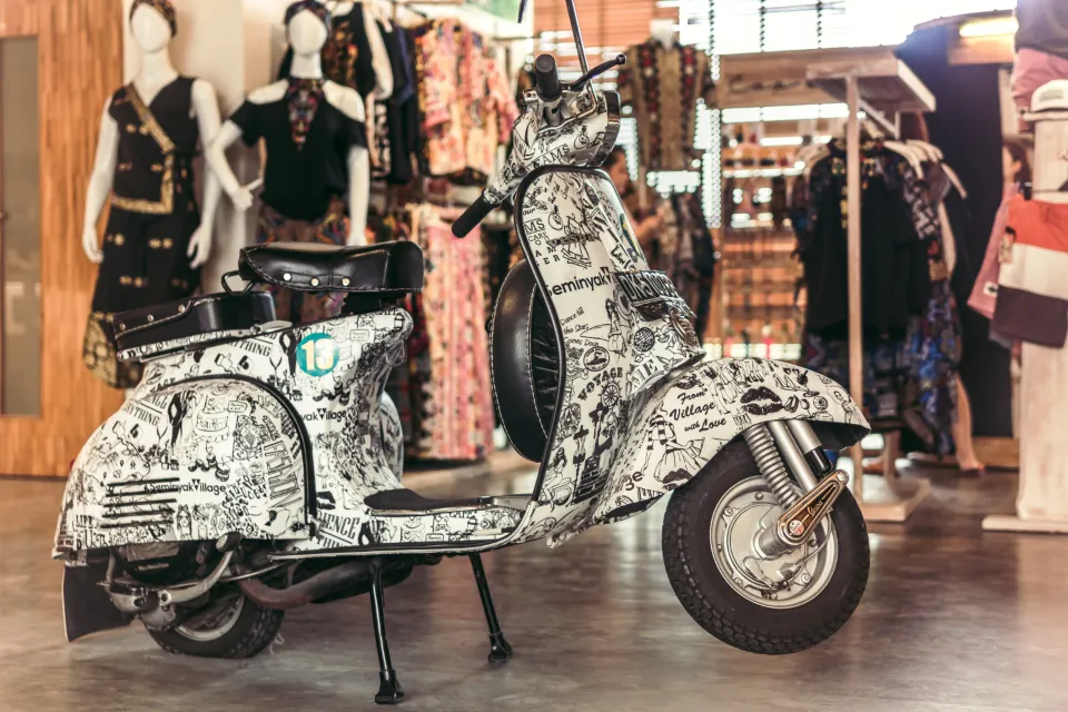 Scooter clássica de cor clara com assento preto, encostada a um muro numa loja decorada