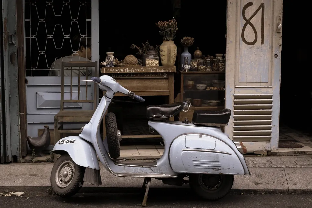 Scooter clássica de cor azul-clara estacionada junto a uma loja de rua com mesa de madeira e vasos