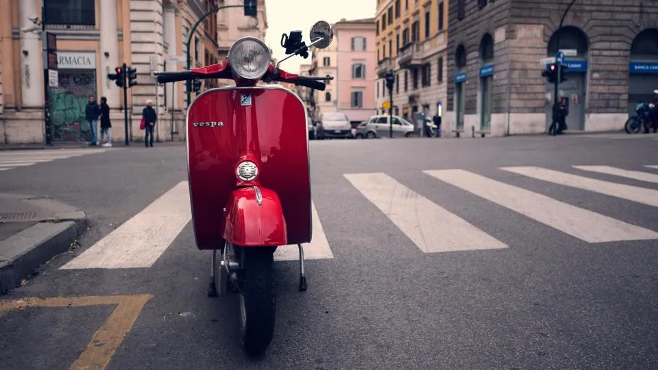 Scooter vermelha estacionada numa rua urbana junto a uma passadeira