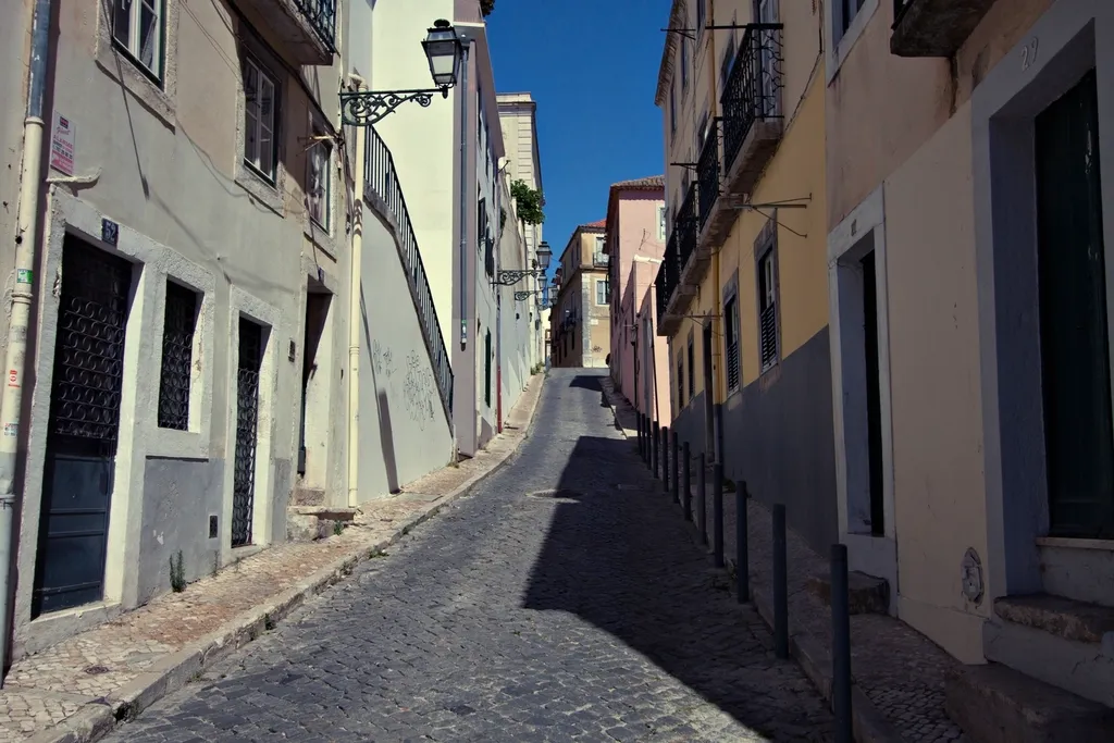 Rua de calçada em subida entre prédios antigos de Lisboa, com candeeiros de ferro e céu azul